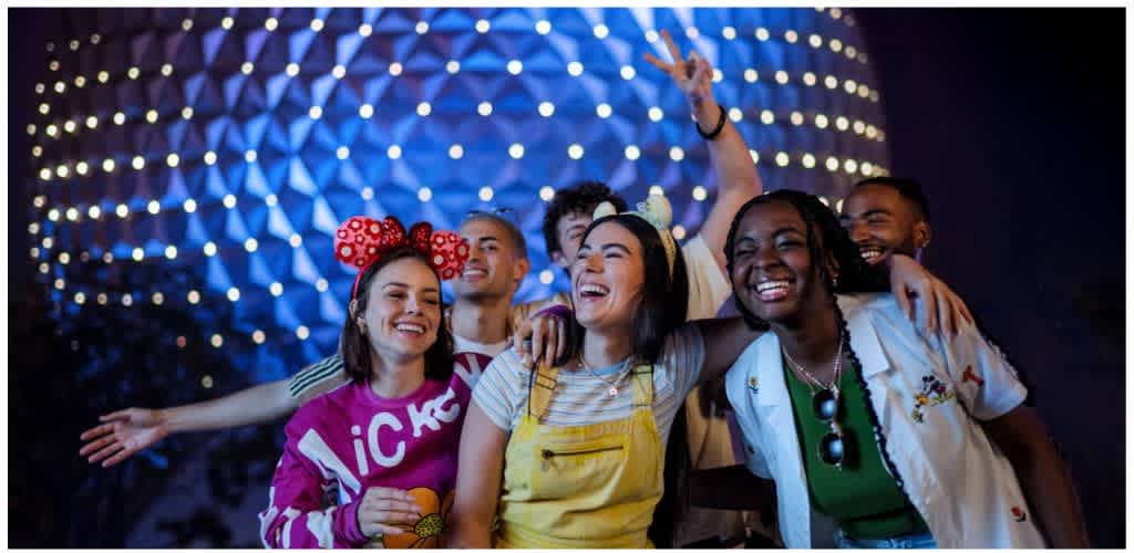 Group of diverse friends smiling and enjoying each other's company at a nighttime event with colorful lights in the background.
