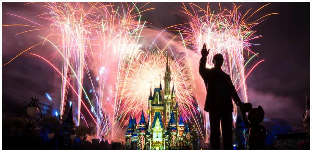 People celebrating a fireworks show at a Disney castle during a nighttime event with colorful explosions illuminating the sky