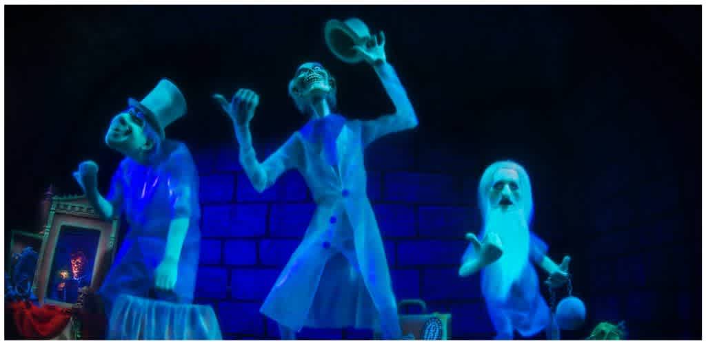Three brightly lit skeleton characters perform on stage with a dark background and brick wall. They are dressed in white costumes and are animated with expressive poses.