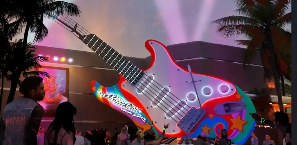 A large colorful guitar-shaped ride with bright lights and star patterns, surrounded by people at an outdoor amusement park during evening twilight.