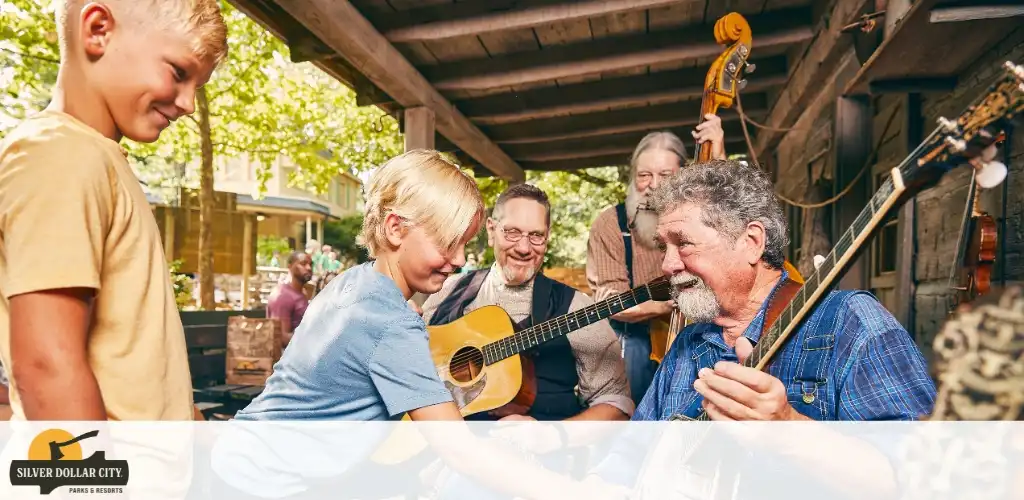 Group of people playing guitars and enjoying music outdoors under a wooden shelter with trees in the background