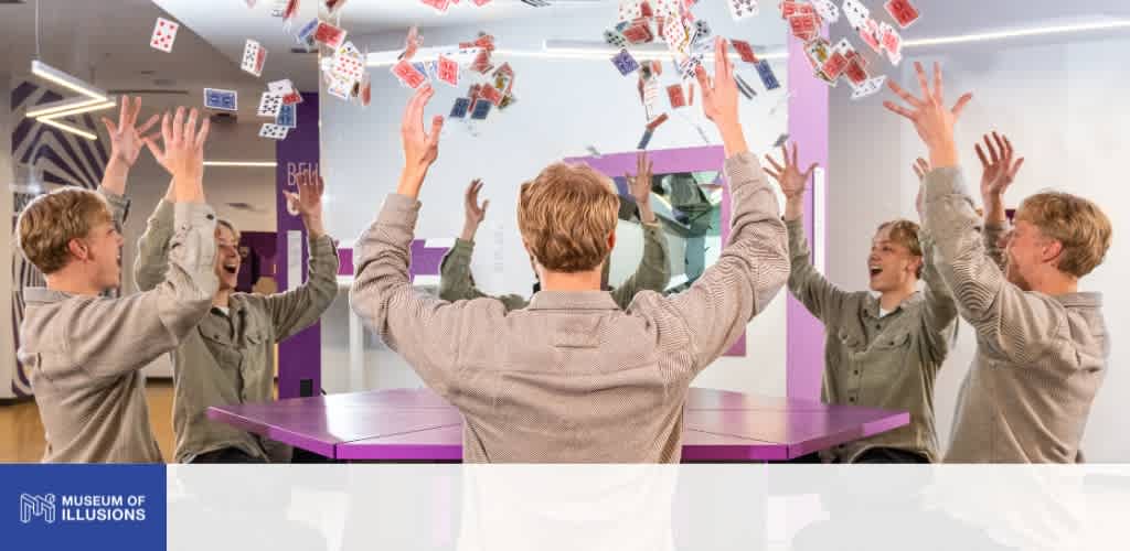 Group of five people throwing playing cards into the air in a room with purple accents and bright lighting