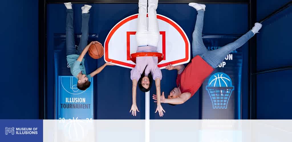 Two children and an adult are upside down on a basketball hoop game machine at the museum of illusions; they are smiling and having fun.
