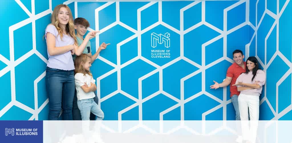 Group of four people standing in front of a blue geometric wall with the Museum of Illusions Cleveland logo.