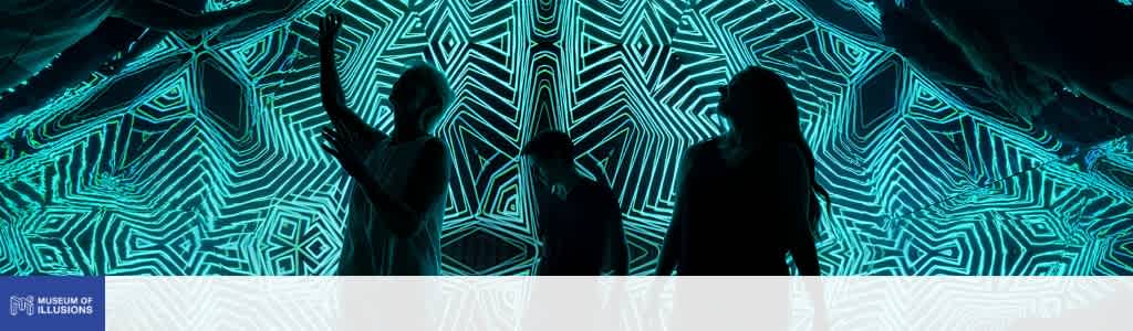 Three people stand in front of a vibrant blue and black geometric light display at the Museum of Illusions.