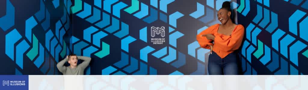 A woman and a boy are smiling and laughing indoors with a geometric blue background at the museum of illusions.