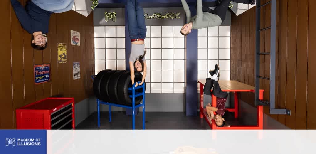Two children and two adults upside down in an illusion room with tires and colorful furniture at the Museum of Illusions