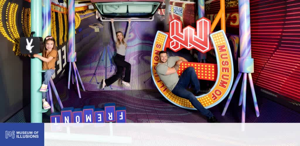 People posing with museum of illusions signage and photo props inside an amusement exhibit with colorful lighting and decorations