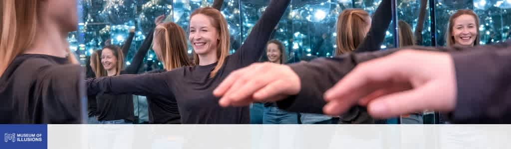Multiple women smiling and holding hands in a mirrored room with blue lighting at Museum of Illusions