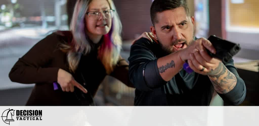 Two people, a woman and a man, appear to be in a tense situation with the man aiming a firearm, while the woman points a gun at him.