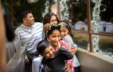 A group of children and adults enjoy a fun outdoor zoo experience together smiling and interacting near an animal enclosure