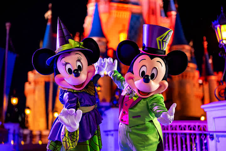 Costumed Mickey and Minnie Mouse characters dressed in colorful Halloween and spring outfits at a theme park during nighttime.