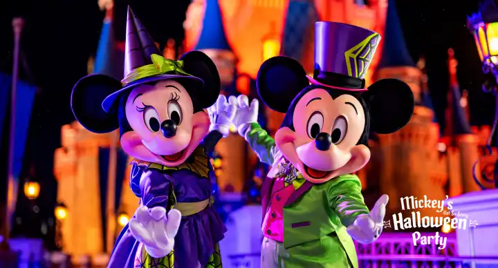 Costumed Mickey and Minnie Mouse characters dressed in colorful Halloween and spring outfits at a theme park during nighttime.