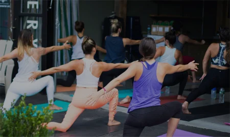 Group of people participating in an outdoor yoga class on mats with instructor leading the session.