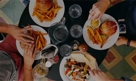 Top-down view of two people sharing a meal at a table, enjoying burgers and fries with drinks in a casual dining setting.