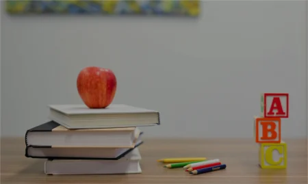 Stack of notebooks with an apple on top, colorful pencils, and ABC blocks on a desk.