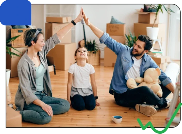 A family of three high-fives each other sitting on a hardwood floor amid moving boxes in a bright, cheerful living room.