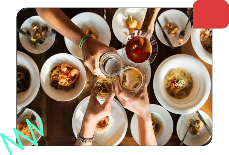 People clinking glasses of drinks above plates of food at a table in a restaurant.