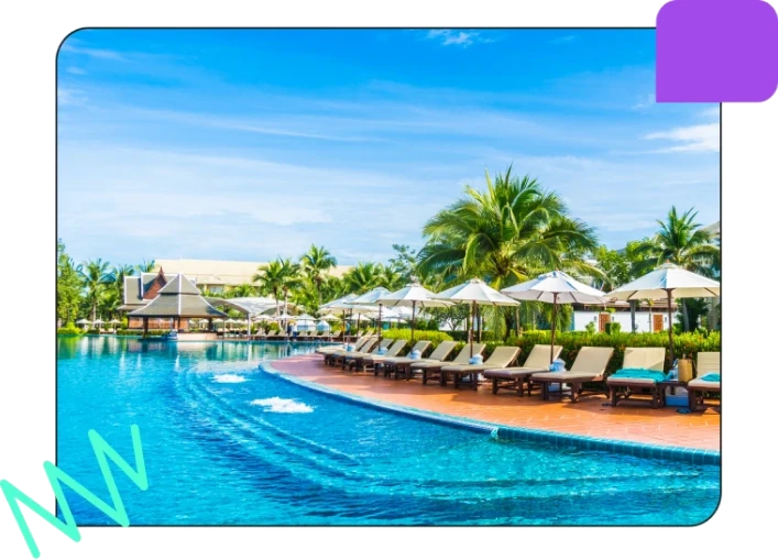 A luxurious outdoor pool area with lounge chairs, umbrellas, palm trees, and a clear blue sky, perfect for relaxation and leisure.